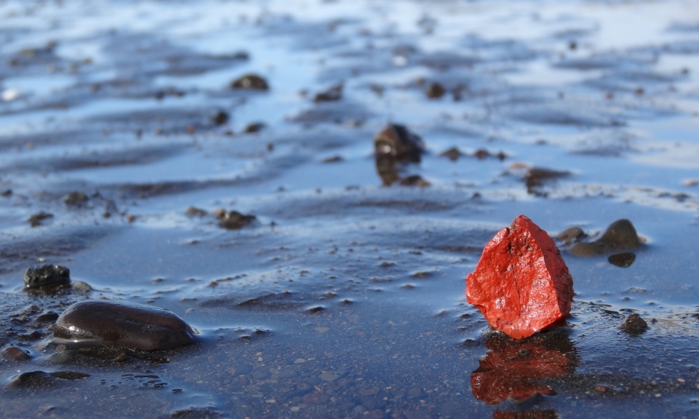 un cailloux rouge sur sable noir mouillé